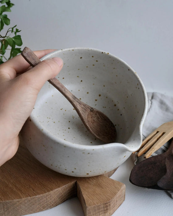 White ceramic matcha bowl being held by a hand, with wooden spoon on a wooden surface
