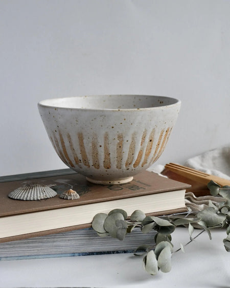 Cream speckled ceramic bowl on books with eucalyptus leaves and seashells on a light background