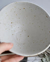 White ceramic bowl with a speckled pattern held by a hand against a neutral background