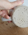 Hand holding a cream speckled textured ceramic mug over a wooden surface