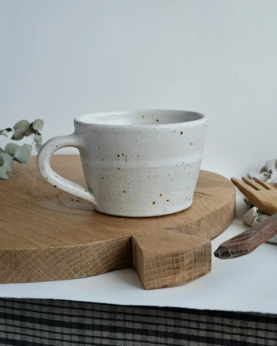 Speckled ceramic mug on a wooden chopping board with a white background