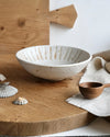 White ceramic bowl on a wooden surface with a wooden spoon and shells.