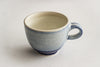A blue glazed handmade ceramic mug with a rustic style, showing glaze drips and other perfect imperfections, on a white background.