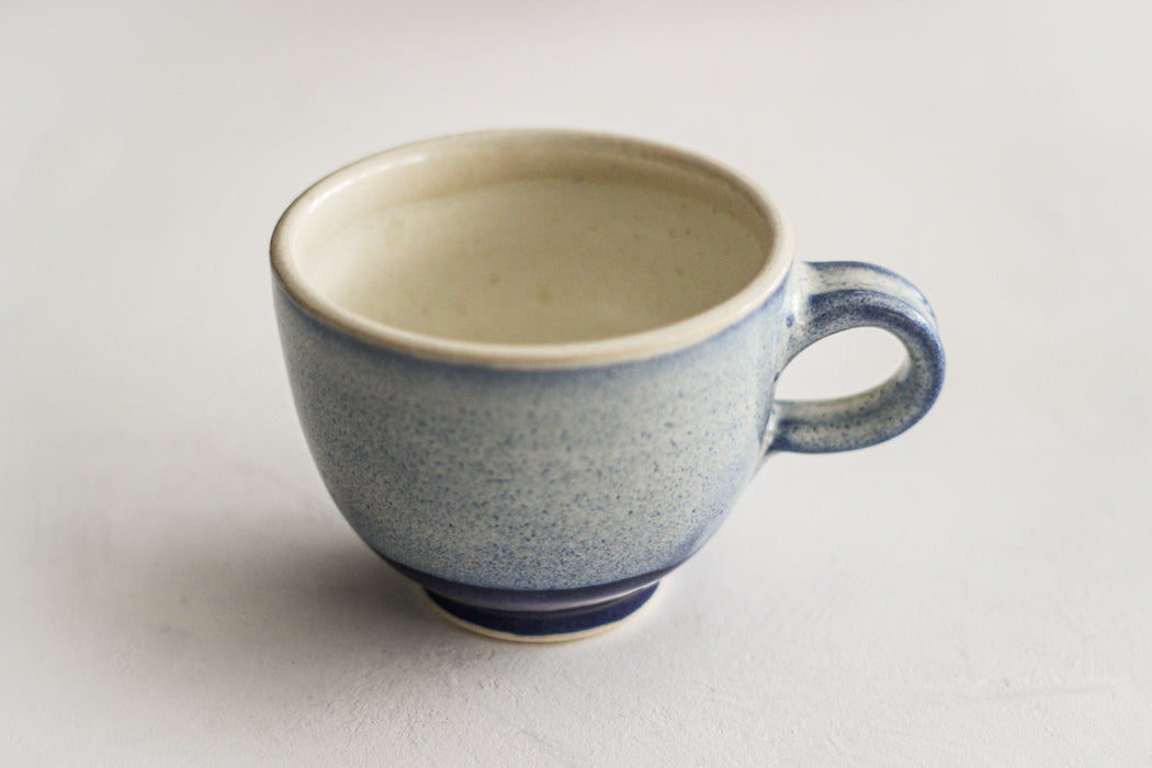 A blue glazed handmade ceramic mug with a rustic style, showing glaze drips and other perfect imperfections, on a white background.