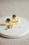 Gold stud earrings with iolite stones on a white plate