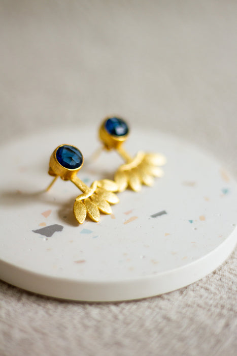 Gold stud earrings with iolite stones on a white plate