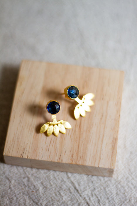 Gold stud earrings with iolite stones on a wooden block