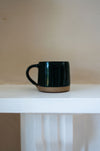 Dark green mug on a white table with a cream background