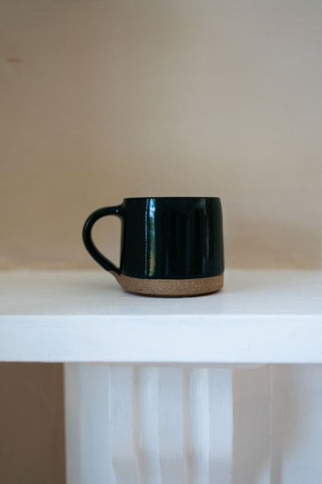 Dark green mug on a white table with a cream background