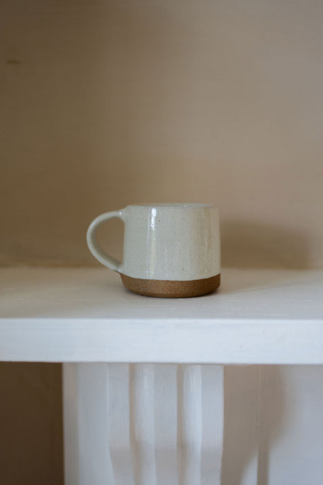 White ceramic mug with brown base on a white surface against a beige wall