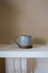 pale blue ceramic mug on a white table with a cream background