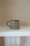 Ceramic mug with speckled brown design on a white table with a beige background