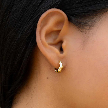 Close-up of a models ear wearing a gold hoop earring with dark hair and a green background