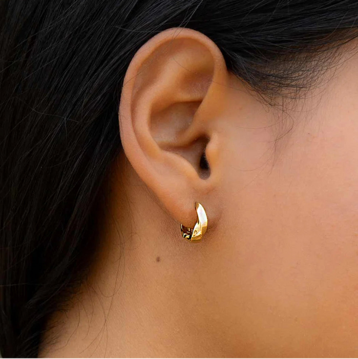 Close-up of a models ear wearing a gold hoop earring with dark hair and a green background
