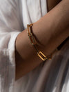 Close up persons wrist wearing a gold link bracelet and a white shirt