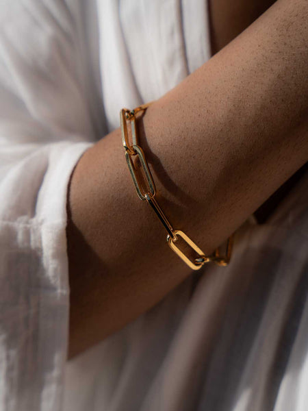 Close up persons wrist wearing a gold link bracelet and a white shirt