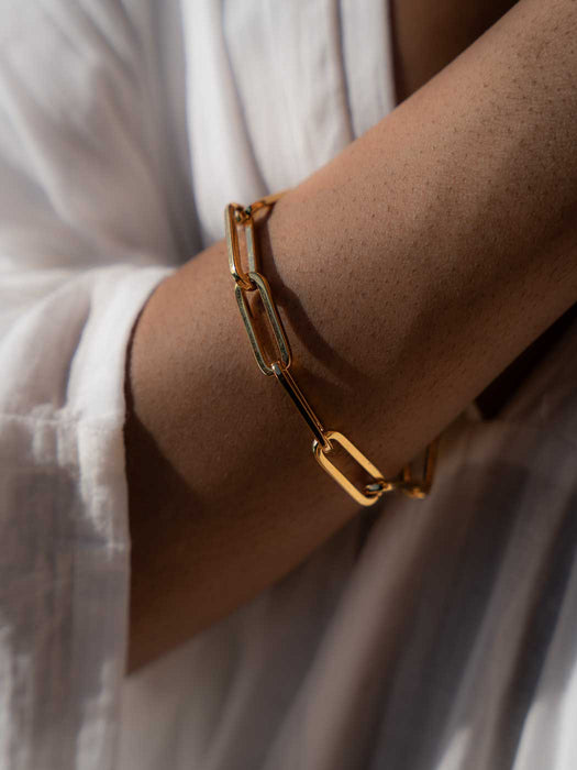 Close up persons wrist wearing a gold link bracelet and a white shirt