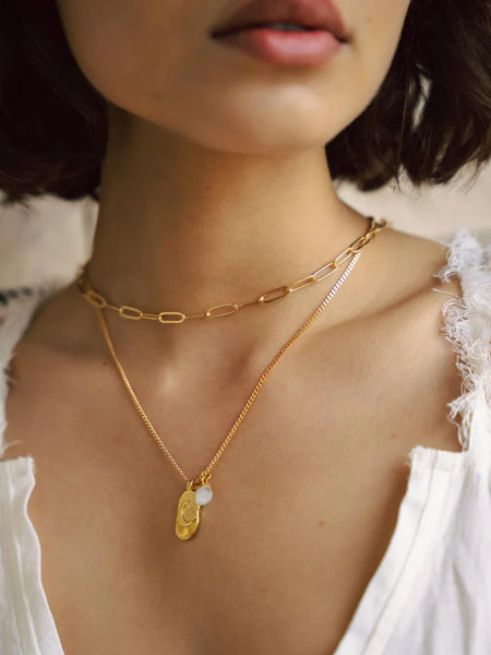 Close-up of a person wearing gold necklaces with a pendant and a white dress