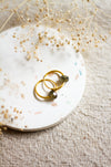 Gold hoop earrings on a white plate with dried flowers on a beige linen surface