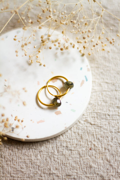 Gold hoop earrings on a white plate with dried flowers on a beige linen surface