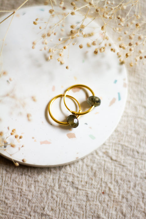 Gold hoop earrings with labradorite bads on a white plate with dried flowers on a beige linen background