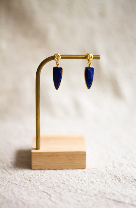 Lapis lazuli earrings on a gold stand with a wooden base against a neutral background
