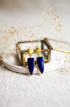 Lapis and gold earrings withon a white dish with a light linen background and dried flowers 