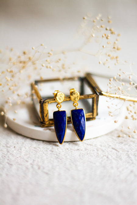 Lapis and gold earrings withon a white dish with a light linen background and dried flowers 