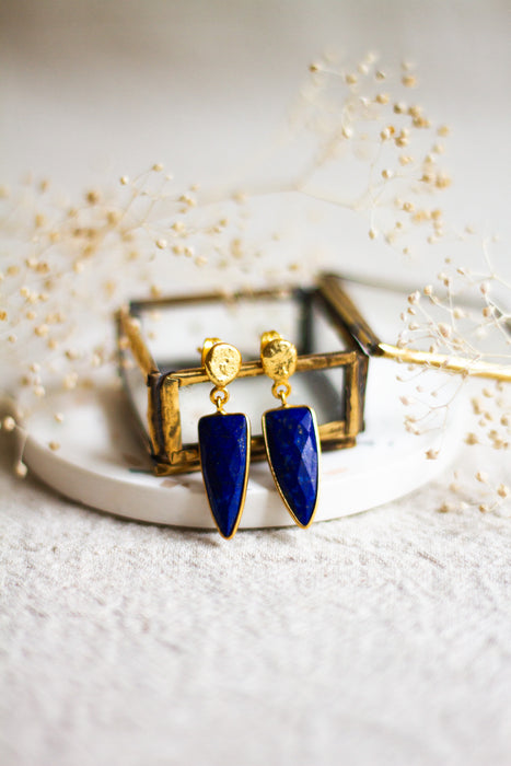 Lapis and gold earrings withon a white dish with a light linen background and dried flowers 