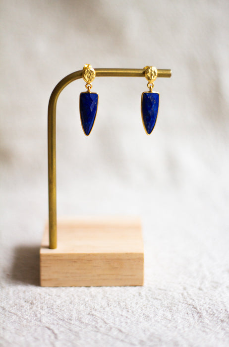 Gold and lapis lazuli earrings on a wooden stand against a light linen background