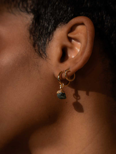 Close up of a persons ear wearing gold and emerald earrings 