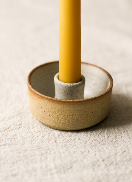 Beige ceramic candlestick holder holding a beeswax candle on a beige linen surface