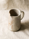 beige ceramic pitcher with a neutral linen background