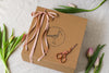 Brown paper package with pink ribbon, scissors, and tulips on a light background