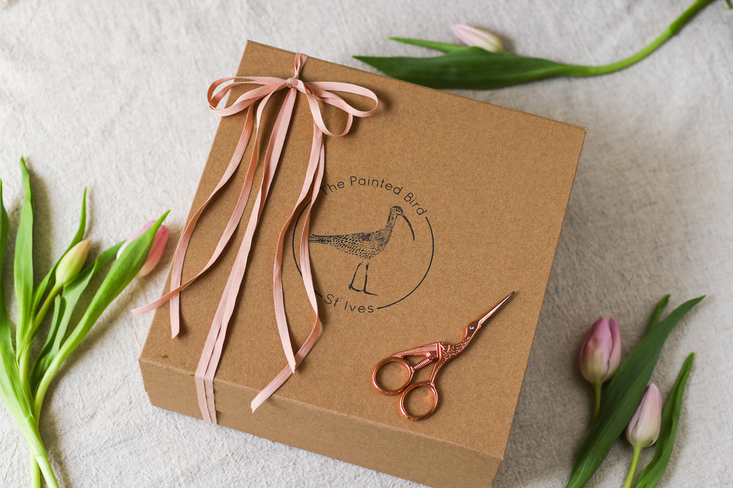 Brown kraft paper gift box with pink ribbon, scissors, and tulips on a light background