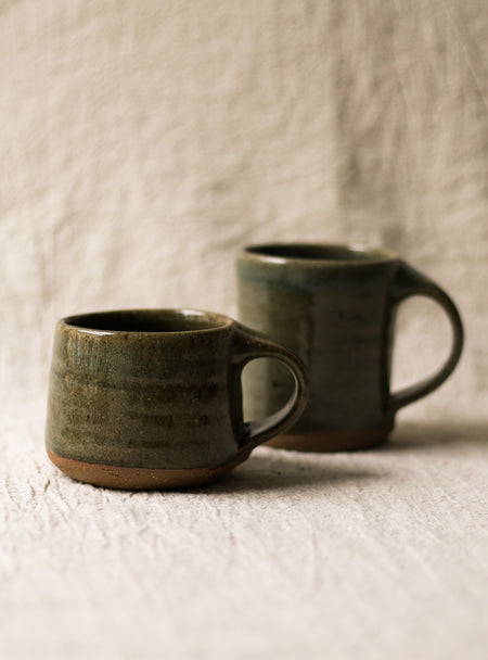 Two green ceramic mugs on a textured beige surface