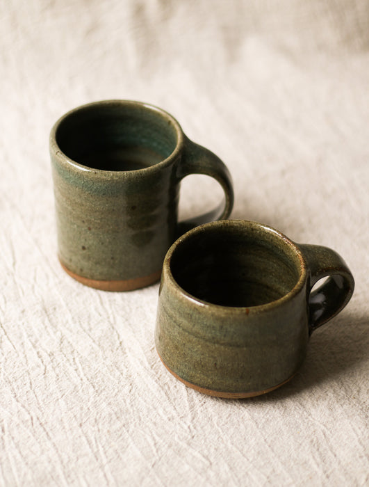 Two green ceramic mugs on a textured beige surface