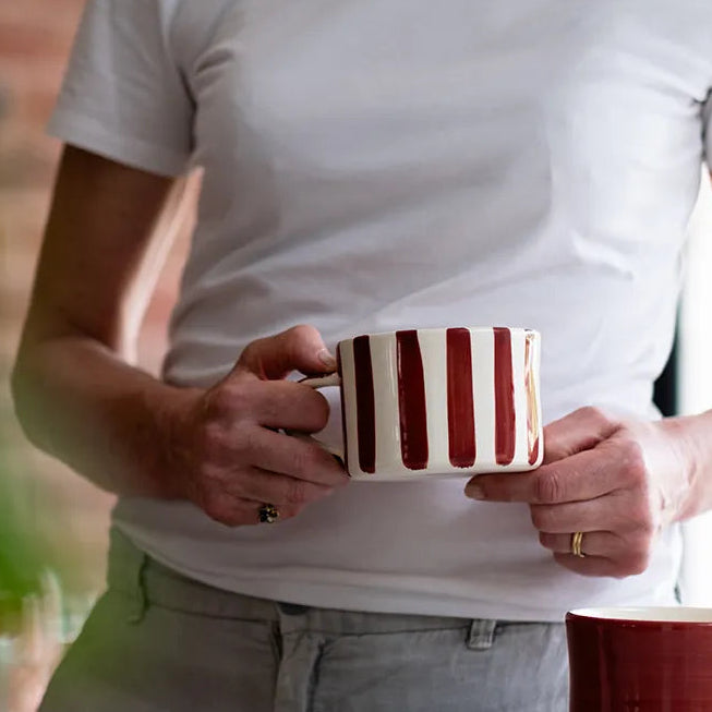 Person holding a striped mug with another mug on a table in a casual setting