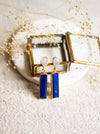 Lapis and moonstone earrings with gold accents on a white coaster with dried flowers.