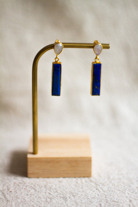Pair of gold earrings with lapis and moonstone on a wooden stand against a neutral background
