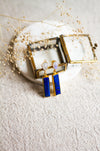 Lapis and moonstone earrings in a glass box, set on a white coaster and a linen surface