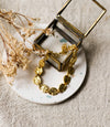 Gold bracelet on a white coaster with dried flowers and a small glass jewellery box and dried flowers in the background.