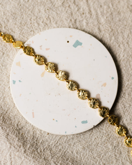 Gold bracelet on a round, speckled coaster with a beige linen background