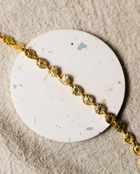 Gold bracelet on a round, speckled coaster with a beige linen background