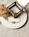Gold bracelet with blue beads on a white coaster with dried flowers and a gold jewellery box.