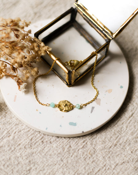 Gold bracelet with blue beads on a white coaster with dried flowers and a gold jewellery box.