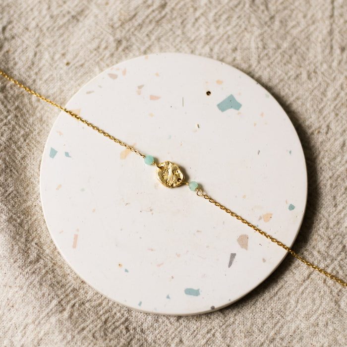 Gold bracelet with gemstone beads on a round, speckled coaster