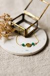 Gold bracelet with green beads on a white coaster with dried flowers and a gold jewellery box.