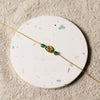 Gold bracelet with green beads on a round, speckled coaster.