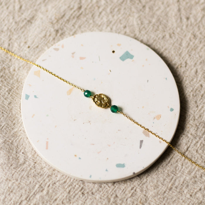 Gold bracelet with green beads on a round, speckled coaster.